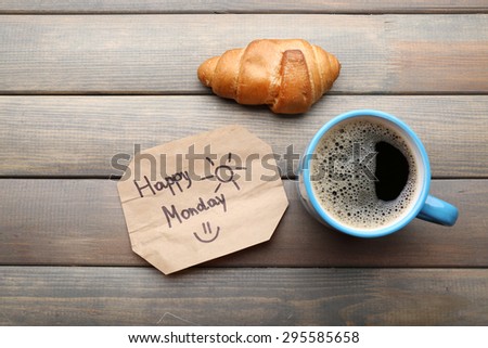 Cup of coffee with fresh croissant and Happy Monday massage on wooden background