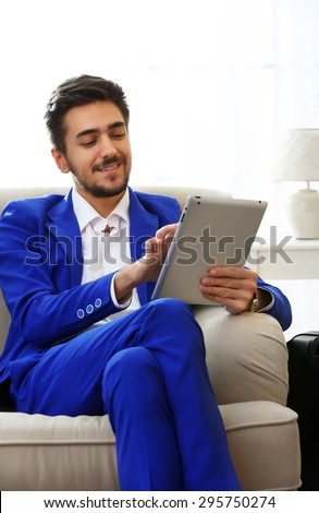 Business man with suitcase and tablet sitting on sofa at home