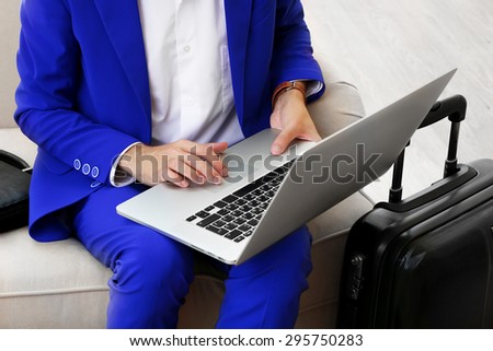 Business man with suitcase and laptop sitting on sofa in hall