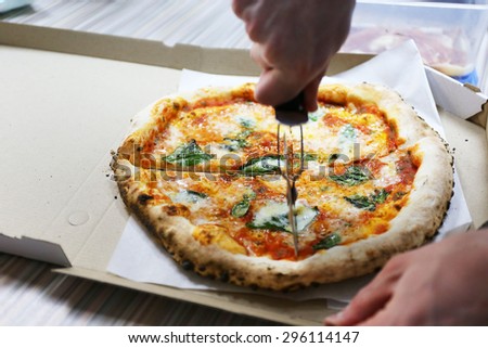 Male hand cutting pizza with blade pizza in box, closeup