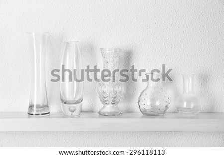 Decorative glass vases on wooden shelf  on white wallpaper background