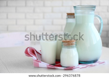 Pitcher, jars and glass of milk on wooden table, on bricks wall background