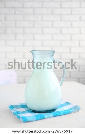 Pitcher of milk on wooden table, on bricks wall background
