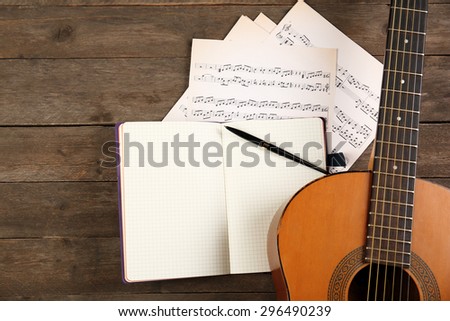 Music recording scene with guitar, notebook and music sheets on wooden table, closeup