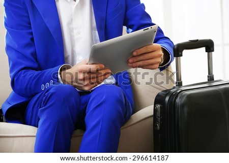 Business man with suitcase and tablet sitting on sofa in hall