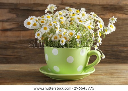 Beautiful bouquet of daisies in cup on wooden background