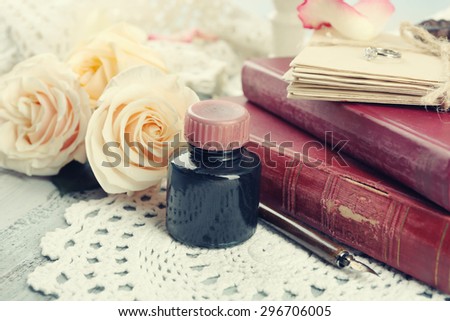 Fresh roses with old book and letters on color wooden table, on light background. Vintage concept