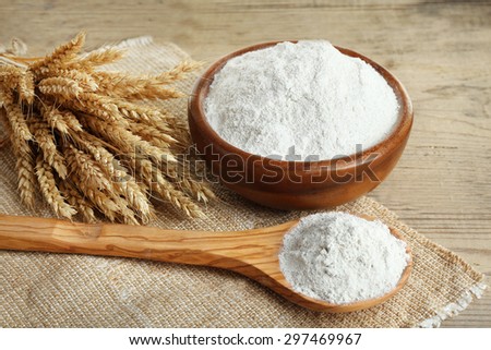 Whole flour in bowl with wheat ears on wooden table, closeup