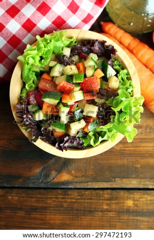 Wooden bowl of fresh vegetable salad on wooden table, top view
