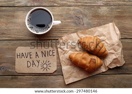 Cup of coffee with fresh croissant and Have A Nice Day massage on wooden table, top view