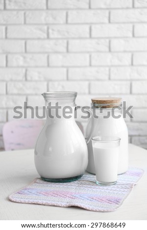 Pitcher, jar and glass of milk on wooden table, on bricks wall background