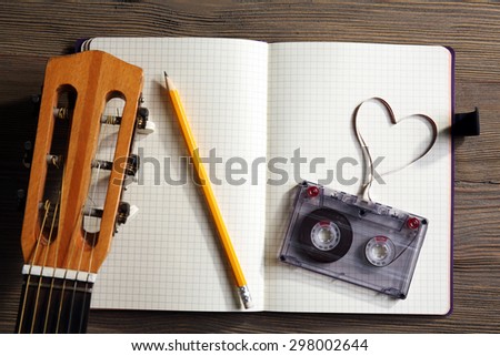 Music recording scene with classical guitar, memo pad and cassette on wooden table, closeup