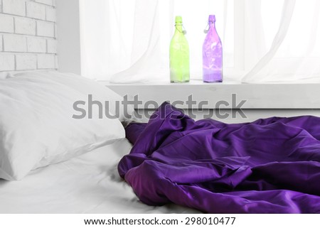 Comfortable bed with purple blanket and pillows in bedroom