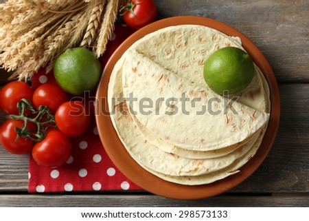 Stack of homemade whole wheat flour tortilla and vegetables on plate, on wooden table background