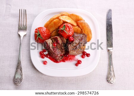 Tasty roasted meat with cranberry sauce and roasted vegetables on plate, on light background