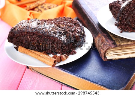Delicious chocolate roll in saucer with spices on wooden table near book, closeup