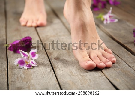 Female feet with flowers on wooden background