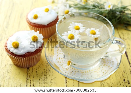 Cup of chamomile tea with chamomile flowers and tasty muffins on color wooden background
