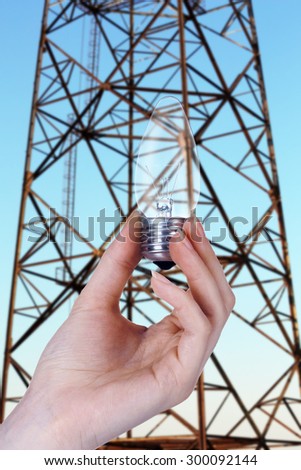 Light bulb in hand on high voltage line background