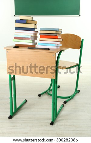 Wooden desk with books and chair in class on blackboard background