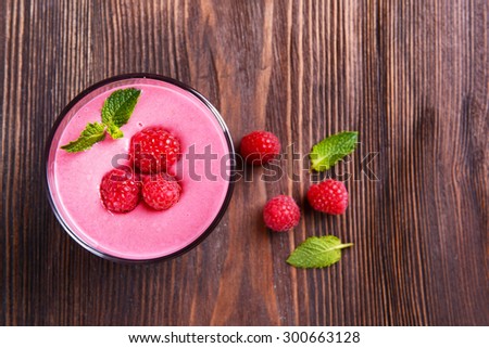 Glass of raspberry milk shake with berries on wooden background