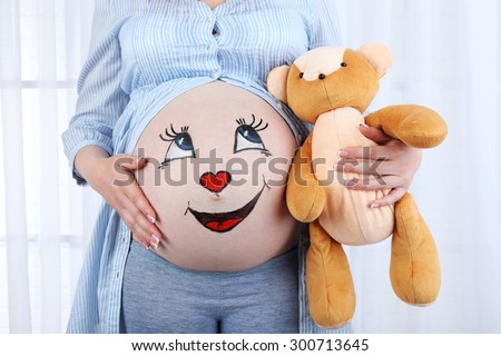 Beautiful young pregnant with baby toy  and picture on her belly, on light background