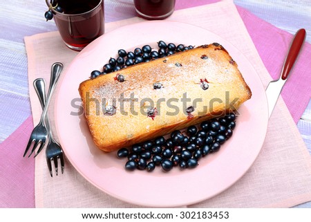 Freshly baked cake with black currants in pink plate on wooden table, top view