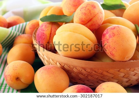 Ripe apricots in wicker bowl on checkered napkin, closeup