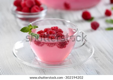 Cup and teapot of raspberry drink with berries on wooden table close up