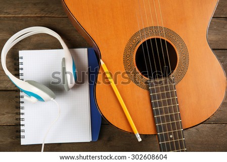 Music recording scene with guitar, memo pad and headphones on wooden table, closeup