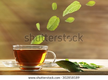 Mint leaves falling in cup of green tea on wooden background