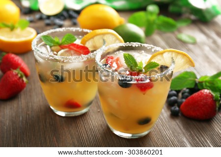 Glasses of berries juice with lemon on wooden table, closeup