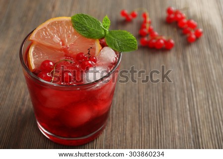 Glass of red currants juice with lemon and ice cubes on wooden table, closeup