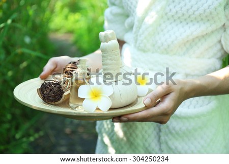 Female hands with tray of spa products over green reeds on river
