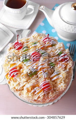 Butter cake with cherries on stand and table setting, on color wooden background