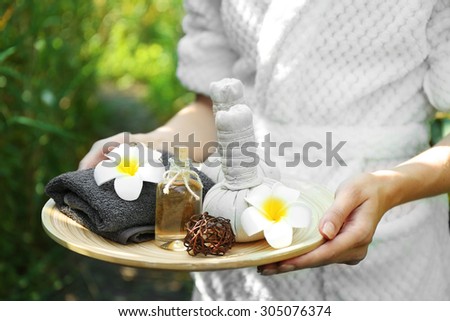 Female hands with tray of spa products over green reeds on river