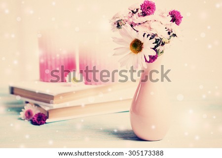 Beautiful flowers in vase and books on table on light background