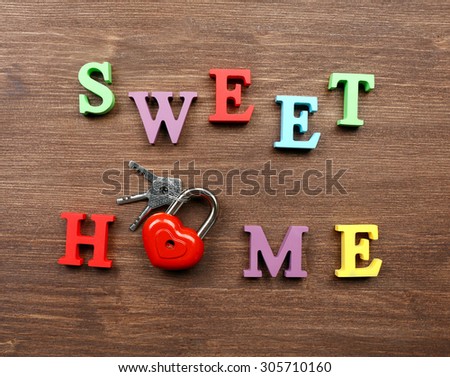 Decorative letters forming words SWEET HOME with lock and keys on wooden background