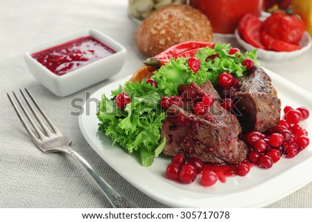 Tasty roasted meat with cranberry sauce on plate, on light background