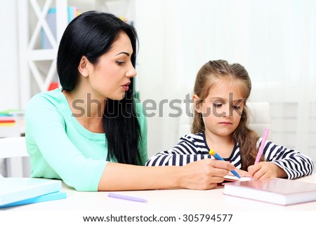 Beautiful school girl doing homework with mother at home