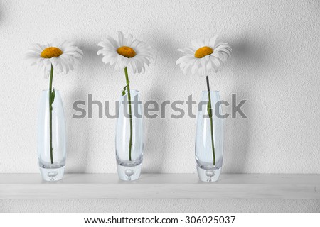 Decorative glass vases with flowers  on wooden shelf  on white wallpaper background