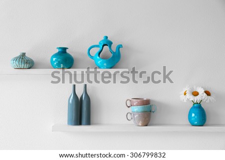 Decorative vases with flowers on wooden shelf  on white wallpaper background