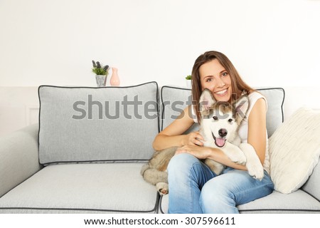 Woman sitting with her malamute dog on sofa in room