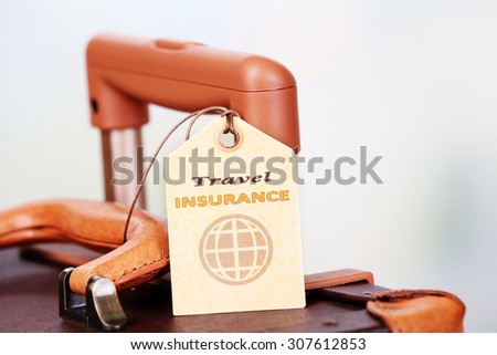 Suitcase with TRAVEL INSURANCE label on light blurred background