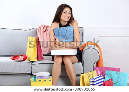 Beautiful young woman with shopping bags and boxes sitting on sofa in room