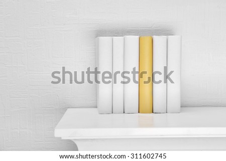 Blank books and yellow one on shelf on white wallpaper background