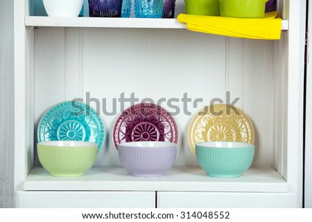 Clean glasses, plates and cutlery on shelf in kitchen cupboard