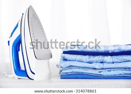 Electronic ironing and pile of clothes on board on curtains background
