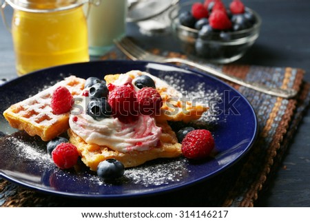 Sweet homemade waffles with forest berries and cream on plate, on dark wooden background