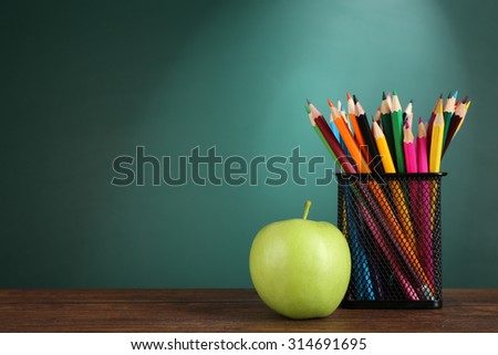 metal holder with crayons and green apple on desk on green chalkboard background